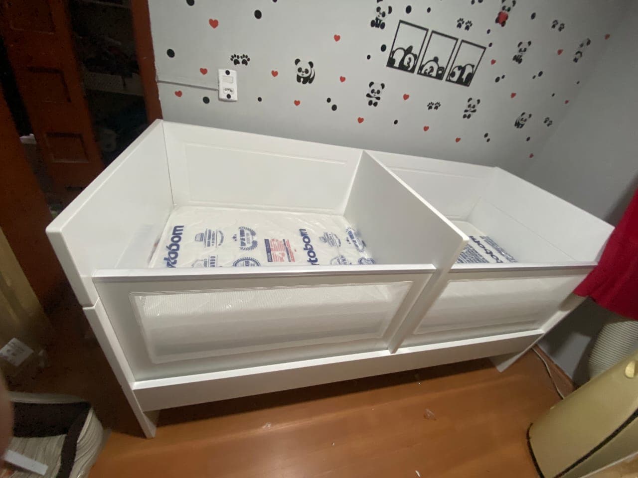 Berço branco montado em quarto de bebê com parede decorada de pandas