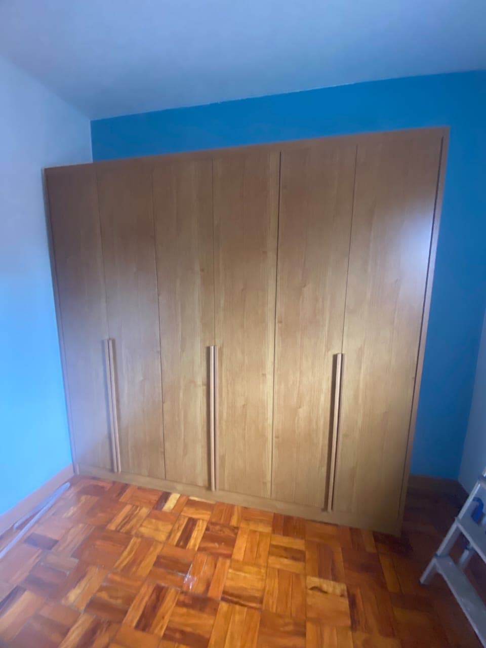 Guarda-roupa amadeirado de seis portas em quarto de parede azul, com piso de taco